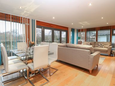 A living room and dining area with glass table white chairs and beige sofas at Tealby Horning