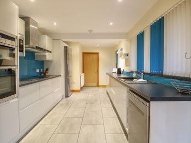 A modern kitchen with white cabinets blue backsplash and tiled floor at Tealby in Horning