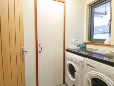 A utility room with washing machine dryer ironing board and a window at Tealby in Horning