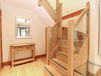 A wooden staircase with glass panels beside a wooden console table with a mirror above it at Tealby in Horning