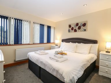 A bedroom with a large bed white linens nightstands with lamps and vertical blinds on windows at Tealby in Horning