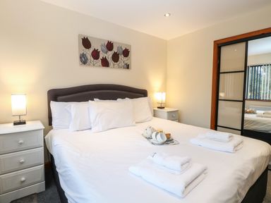A bedroom with a large bed white linens bedside tables with lamps and a floral painting on the wall at Tealby Horning