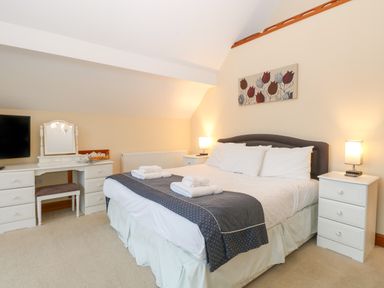 A bedroom with a double bed bedside tables lamps a dressing table and a wall painting at Tealby Horning