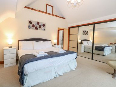 A bedroom with a large bed white bedding and folded towels bedside tables lamps and mirrored wardrobe at Tealby in Horning
