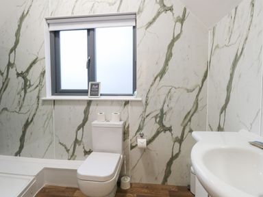 A bathroom with a toilet a sink and a window with marble patterned walls at Tealby in Horning