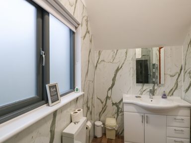 A bathroom with a window a toilet a sink with a mirror and storage cabinets at Tealby in Horning