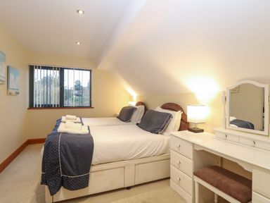A bedroom with two beds side by side a white dressing table with mirror and a window with vertical blinds at Tealby in Horning
