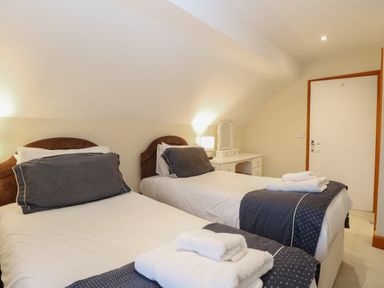 A bedroom with two single beds with dark pillows and throws a white dressing table and door at Tealby in Horning