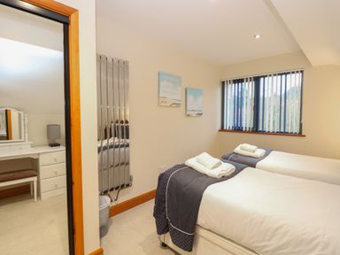 A bedroom with two single beds with towels and navy blue throws a window with vertical blinds a radiator and a vanity table with a bench at Tealby in Horning