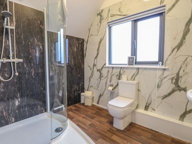 A bathroom with a shower, toilet, trash bins, and a window at Tealby in Horning