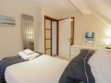 A bedroom with a bed linens and towel on top a white dressing table with a mirror and a lamp at Tealby in Horning