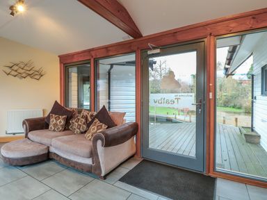 A seating area with a sofa and cushions near a glass door with wooden frame at Tealby in Horning