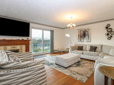A living room with sofas a wooden floor a fireplace a large window and a chandelier at White Gables in Horning