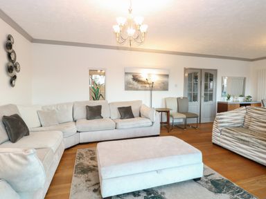 A living room with sofas chairs an ottoman a rug wall art and a chandelier at White Gables in Horning