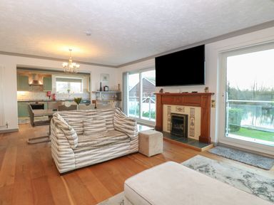 A living room with patterned sofa a fireplace and mounted tv overlooking a garden at White Gables in Horning