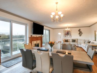 A dining area with a table and chairs next to a living room with sofas a fireplace and a wall-mounted TV at White Gables in Horning