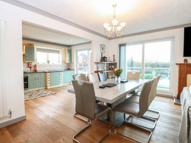 A dining room with a large table and chairs next to a kitchen and sliding glass doors at White Gables in Horning