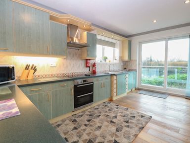 A kitchen with green cabinets a stove a microwave and a sliding glass door overlooking greenery at White Gables in Horning