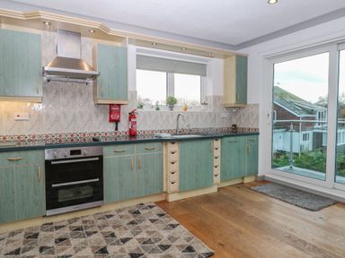 A kitchen with green cabinets a stove a oven a sink fire extinguisher and a sliding glass door at White Gables in Horning