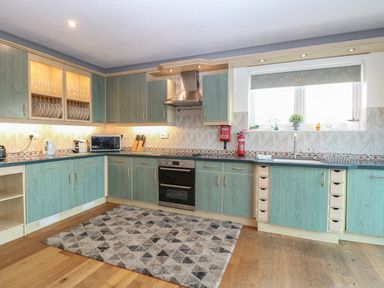 A kitchen with cabinets a stove a microwave a kettle a toaster and a rug on the floor at White Gables in Horning