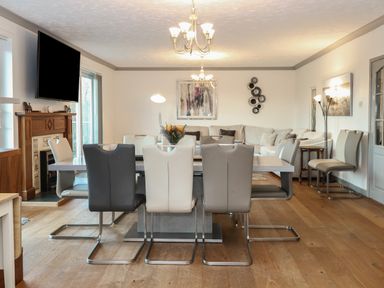 A dining room with a table and mixed color chairs next to a living area with a sofa and a fireplace at White Gables in Horning