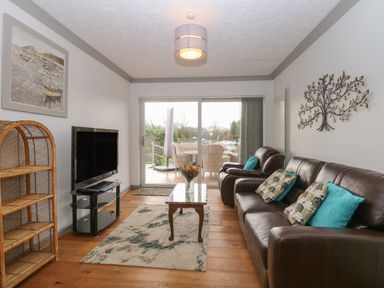 A living room with leather sofas coffee table TV and sliding glass doors to a patio at White Gables in Horning