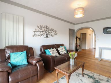 A living room with brown leather sofas blue and patterned cushions a wooden coffee table with flowers and an archway leading to a hallway at White Gables in Horning