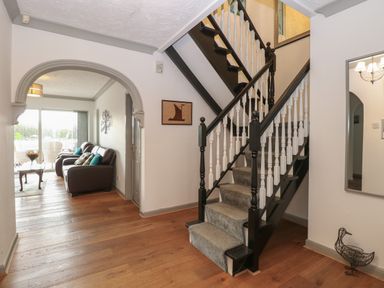 An entrance hall with wooden flooring and a black and white staircase leading upstairs with a view of a living room through an archway at White Gables in Horning