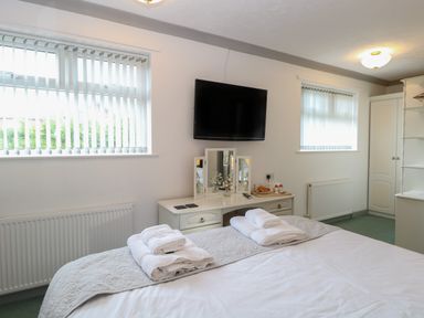 A bedroom with a bed with white linens towels TV and a dressing table with a mirror at White Gables in Horning