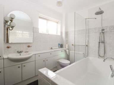 A bathroom with a bathtub and shower, sink with a mirror, toilet, and storage cabinets at White Gables in Horning
