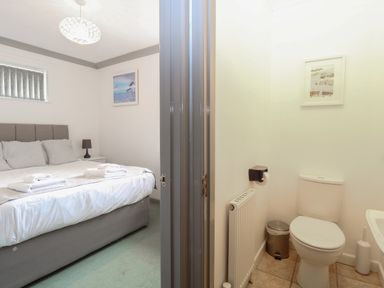 A bedroom with a bed and a lamp next to a small bathroom with a toilet and a trash can at White Gables in Horning
