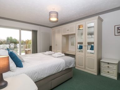 A bedroom with a double bed two bedside tables a wardrobe with mirrors and sliding glass doors showing an outdoor view at White Gables in Horning