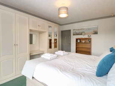 A bedroom with a double bed with blue and white pillows and white towels on top with built in wardrobes and a wooden bookshelf at White Gables in Horning