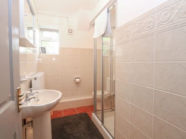 A bathroom with a pedestal sink a radiator a window a toilet a shower with glass doors and a dark floor mat at White Gables in Horning
