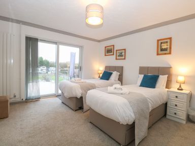 A bedroom with two single beds with white bedding and blue cushions bedside tables lamps and framed pictures on the wall at White Gables in Horning
