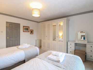 A bedroom with two single beds folded towels on the beds a wardrobe a dressing table a cushioned stool and a closed door at White Gables in Horning