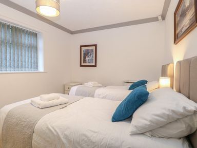 A bedroom with two single beds with blue cushions and folded towels on a grey runner at White Gables in Horning