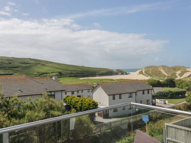 A view of houses with tiled roofs green hills sand dunes and the sea in the background at Atlantic View in Holywell Bay