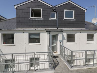 The exterior of a two story house with white walls and dark upper cladding with metal railings at Atlantic View in Holywell Bay