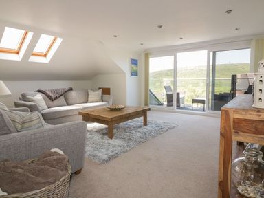 A living room with grey sofas wooden coffee table and sliding glass doors opening to a balcony at Atlantic View in Holywell Bay