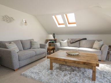 A living room with two gray sofas a wooden coffee table and skylight windows at Atlantic View in Holywell Bay