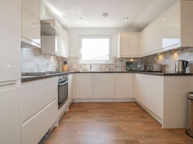 A kitchen with white cabinets a microwave toaster kettle and oven at Atlantic View in Holywell Bay