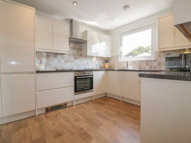 A kitchen with white cabinets stove oven microwave and knife block at Atlantic View in Holywell Bay