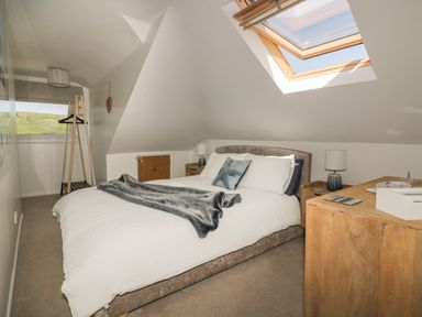 A bedroom with a bed bedside tables a table lamp a wooden dresser and a skylight window at Atlantic View in Holywell Bay