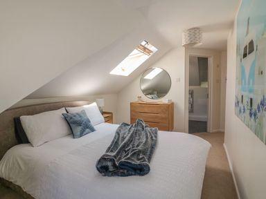 A bedroom with a bed a wooden dresser with a round mirror and a door leading to a bathroom at Atlantic View in Holywell Bay