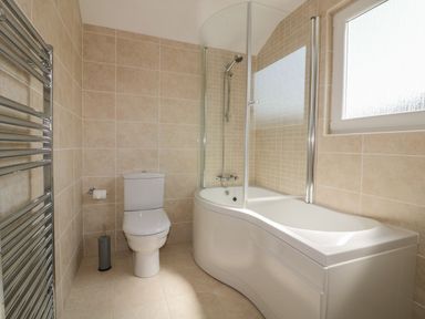 A bathroom with a toilet, a curved bathtub with a shower, and a towel radiator at Atlantic View in Holywell Bay