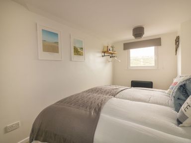 A bedroom with two beds a window and framed pictures on the wall at Atlantic View in Holywell Bay