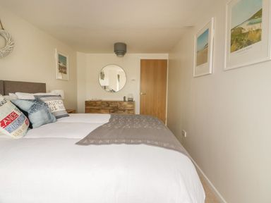 A bedroom with a bed and pillows a wooden dresser with a round mirror and framed pictures on the walls at Atlantic View in Holywell Bay
