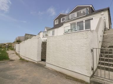 A white exterior wall with metal gates and stairs leading up to a house with balconies at Atlantic View in Holywell Bay