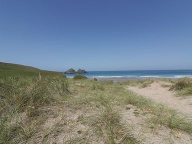 A sandy path with grass leading to the beach and ocean with rocks in the water at Atlantic View in Holywell Bay